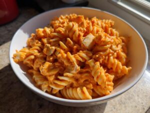 A white bowl filled with creamy, orange-sauced rotini pasta and chunks of chicken, representing the enchilada pasta dish.