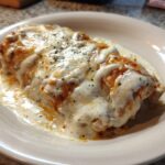 Close-up of a baked dish, likely an enchilada, smothered in melted white cheese and creamy sauce, inspired by fiesta lime chicken flavors.