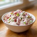 A close-up of creamy hoagie dip mixed with chopped meats, green peppers, and red onion in a white bowl.