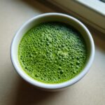 Overhead view of creamy matcha chia pudding in a white bowl, showing vibrant green color and fine foam bubbles.