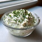 A glass bowl filled with creamy pickle dip, garnished generously with freshly chopped green chives.