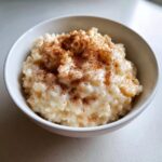 Close-up of creamy rice pudding in a white bowl, generously dusted with cinnamon.