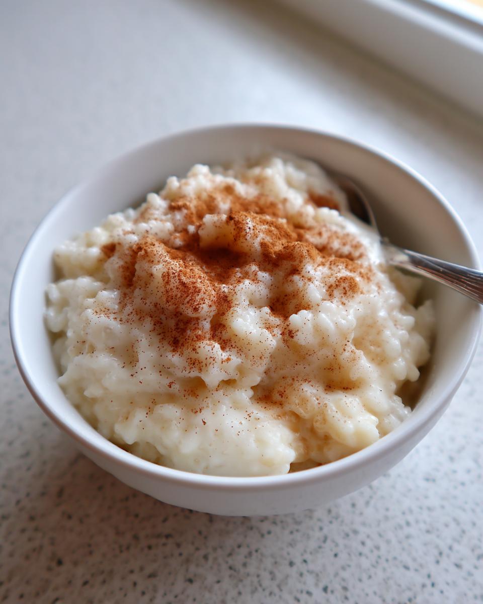 A close-up of creamy rice pudding in a white bowl, generously sprinkled with cinnamon.
