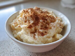 Close-up of a white bowl filled with creamy rice pudding generously sprinkled with ground cinnamon.