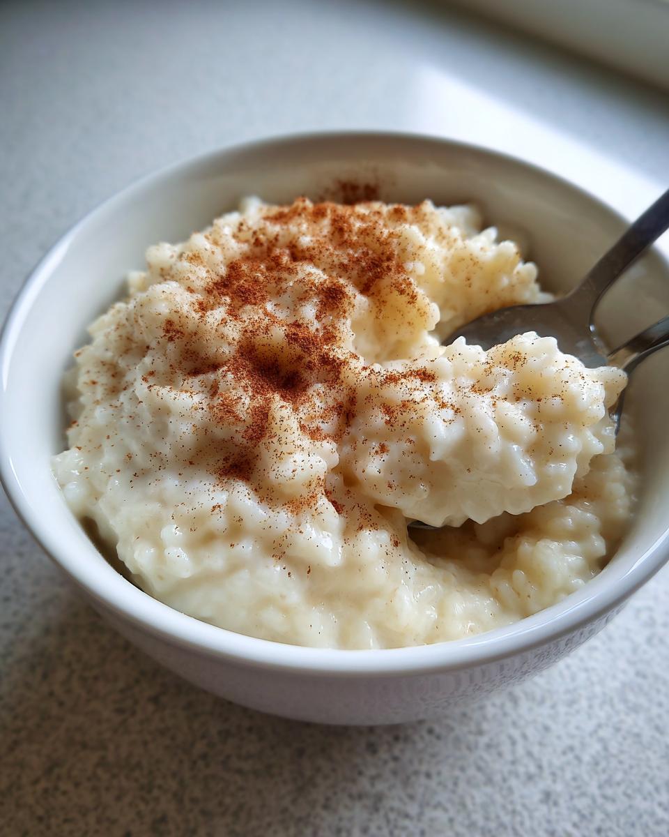 Close-up of creamy rice pudding in a white bowl, generously sprinkled with cinnamon, with a spoon scooping some out.