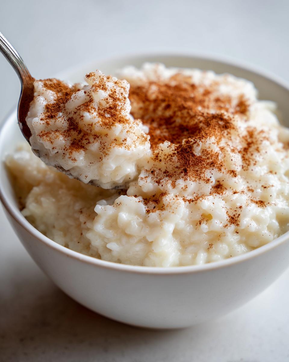 A spoonful of creamy rice pudding topped generously with ground cinnamon being lifted from a white bowl.