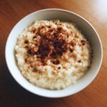 Overhead view of a white bowl filled with creamy rice pudding recipe, generously dusted with cinnamon.