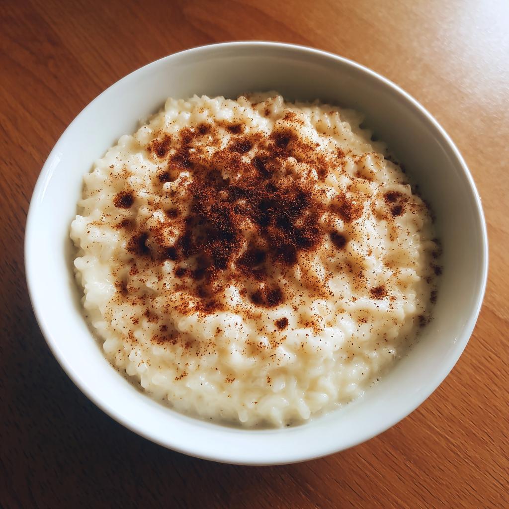 Overhead view of a white bowl filled with creamy rice pudding recipe, generously dusted with cinnamon.