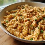 Close-up of creamy tuna pasta made with fusilli noodles and green peas, served in a light-colored skillet.