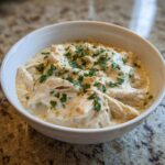 A white bowl filled with creamy white chicken chili topped with fresh chopped parsley.