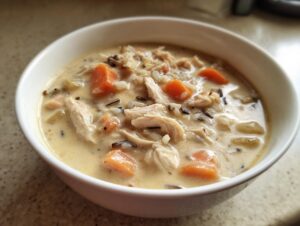 Close-up of a hearty bowl of creamy wild rice soup featuring shredded chicken, bright orange carrots, and wild rice grains.