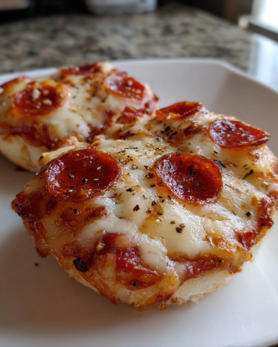 Two small, crispy English muffin pizza halves topped with melted cheese, pepperoni slices, and herbs.