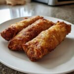 Three perfectly golden brown and crispy egg roll appetizers arranged on a white plate.