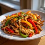 Close-up of shredded crockpot chicken fajitas mixed with colorful bell peppers and onions on a white plate.