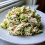 A mound of creamy dill pickle chicken salad featuring shredded chicken and visible chunks of bright green pickles on a white plate.