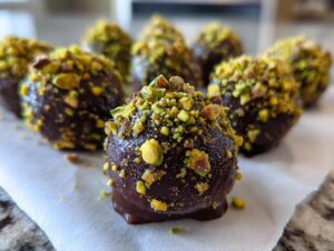 Close-up of rich, dark chocolate Dubai chocolate balls generously coated in chopped green pistachios.