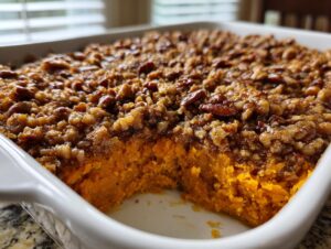 A close-up view of an easy sweet potato casserole in a white baking dish, showing the bright orange filling and crunchy pecan topping.
