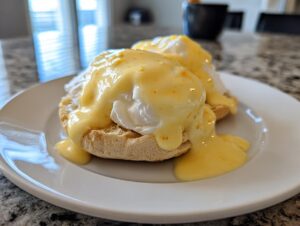 Two eggs benedict halves generously covered with rich, yellow hollandaise sauce, served on a white plate.
