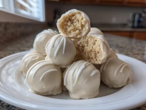 A stack of white chocolate-coated sugar cookie truffles, one broken open to show the crumbly interior.