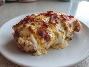A close-up of a juicy chicken breast topped with melted cheese, creamy sauce, and crispy bacon pieces, likely the Fiesta Lime Chicken.