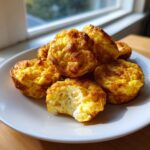 A pile of golden brown, fluffy egg bites served on a white plate, with one egg bite having a bite taken out.