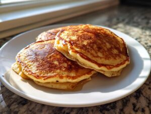 A stack of three golden brown, fluffy banana pancakes drizzled with syrup on a white plate.