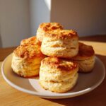 A stack of golden brown, flaky buttermilk biscuits piled high on a light-colored plate.