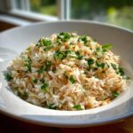 A close-up of fluffy rice pilaf, featuring toasted vermicelli and fresh chopped parsley, served in a white bowl.