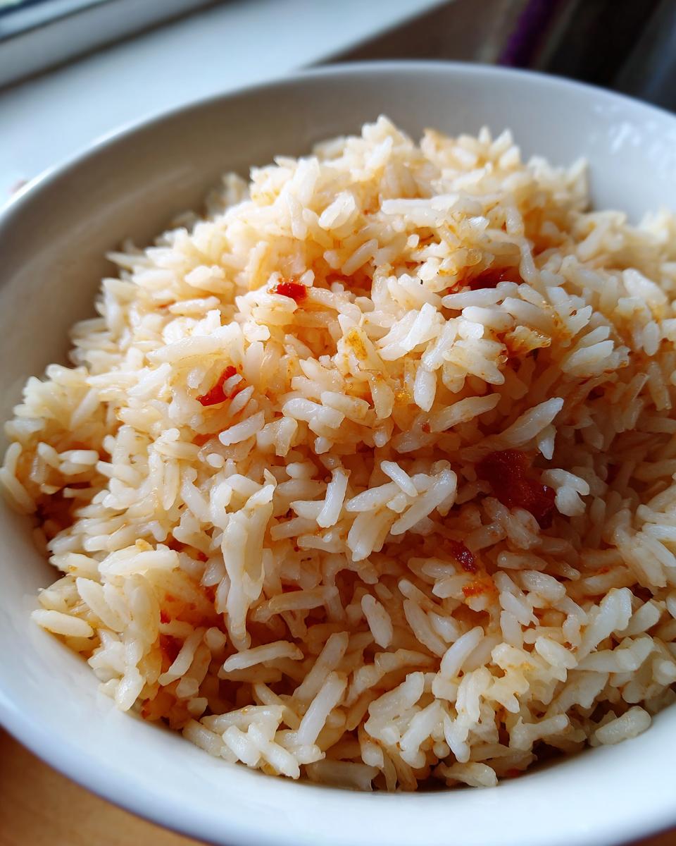Close-up of fluffy white and slightly orange-tinted spanish rice served in a white bowl.