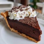 A decadent slice of french silk pie featuring a thick chocolate filling, graham cracker crust, topped with whipped cream and chocolate shavings.