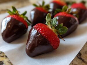 Close-up of fresh chocolate covered strawberries resting on white parchment paper after dipping.