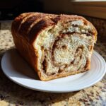 A loaf of homemade raisin bread, sliced to show the cinnamon swirl filling, resting on a white plate.