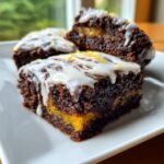 Close-up of fudgy Lemon Brownies squares with a bright yellow center, drizzled with white icing and lemon zest.