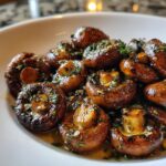 A close-up of glossy, sautéed garlic butter mushrooms garnished with fresh herbs in a white serving bowl.