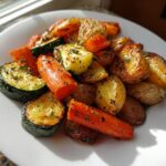 A close-up of perfectly cooked Garlic Herb Roasted Veggies including carrots, zucchini, and small potatoes on a white plate.