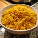A close-up of vibrant yellow garlic turmeric rice perfectly cooked and served in a white bowl.