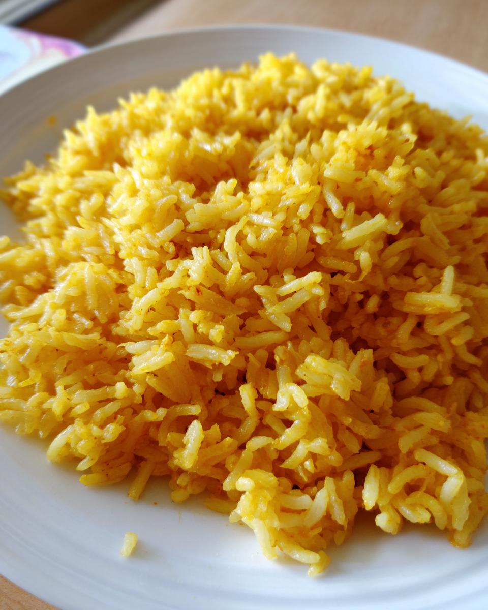 Close-up of fluffy, bright yellow garlic turmeric rice piled high on a white plate.