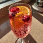 Close-up of a fizzy glass of pink champagne punch garnished with orange slices and fresh raspberries.