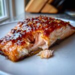 Close-up of a perfectly cooked baked salmon recipe fillet with a thick, glistening, caramelized glaze being flaked open.
