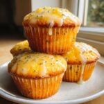 A stack of three golden lemon poppy seed muffins topped with a thick lemon glaze and zest.