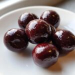 Close-up of several glossy, dark red chocolate covered cherries resting on a white plate.