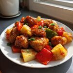 Close-up of glazed, crispy chicken pieces mixed with pineapple chunks and bell peppers, reminiscent of Hawaiian chicken sheet pan style.