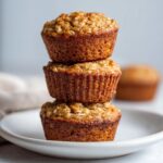 A stack of three golden brown, healthy oatmeal muffins sitting on a white plate.