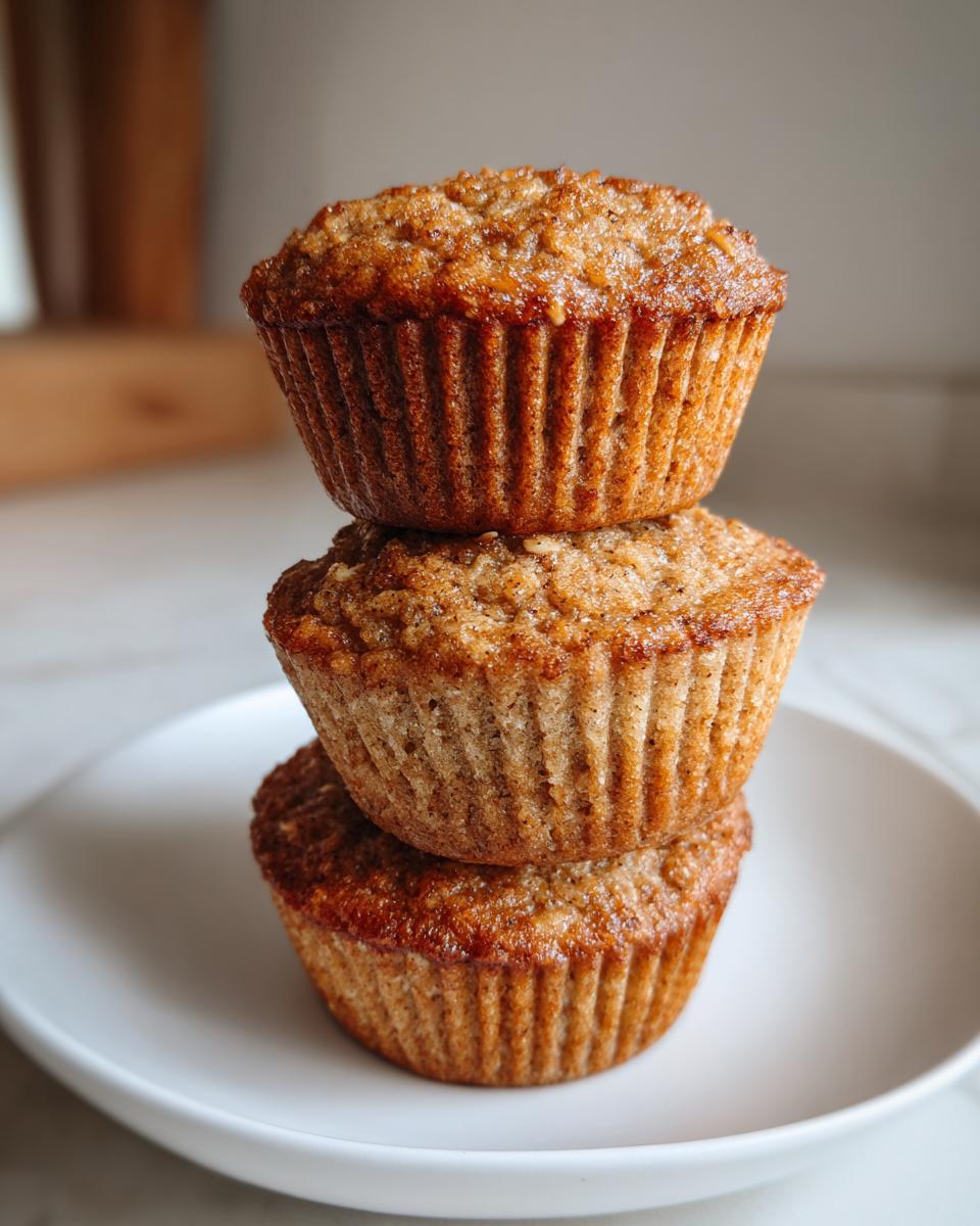 Three golden brown oatmeal muffins stacked vertically on a small white plate.