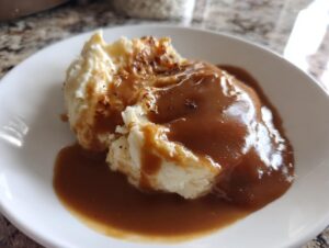 A close-up of fluffy mashed potatoes generously covered in rich, smooth homemade brown gravy on a white plate.