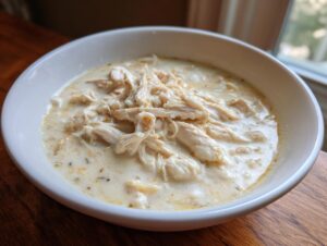 Close-up of a white bowl filled with rich, creamy cream of chicken soup topped with shredded chicken.