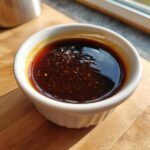 Close-up of thick, dark homemade teriyaki sauce with visible spice flecks in a small white ramekin.