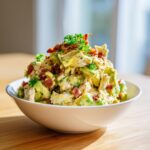 A generous serving of creamy honey mustard chicken salad mixed with avocado chunks and topped with crispy bacon bits and parsley.