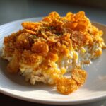 A close-up serving of creamy hot chicken salad casserole topped with crunchy, golden cornflakes.
