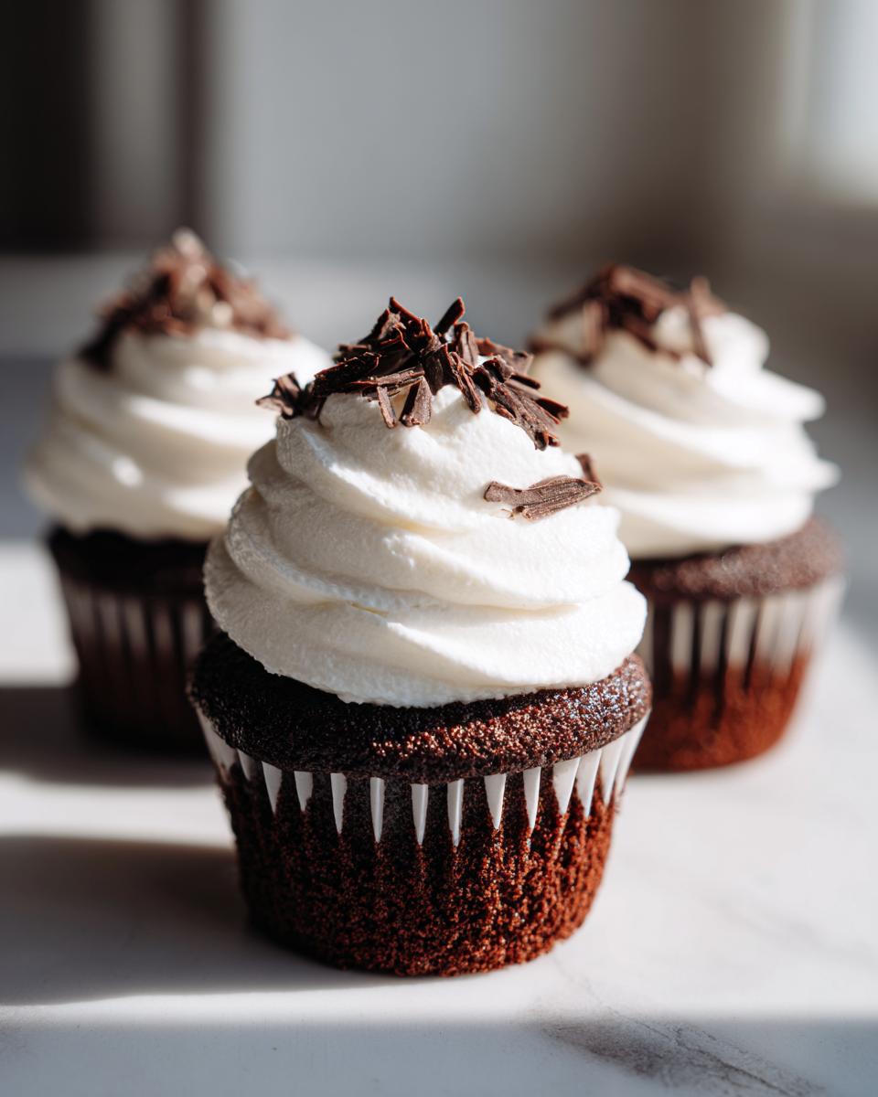 Three rich chocolate hot chocolate cupcakes topped with swirled white frosting and dark chocolate shavings.